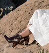A woman in a white Isla dress sitting on a rock by Bed Stu.