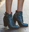 A woman wearing a pair of blue Bed Stu Isla ankle boots.