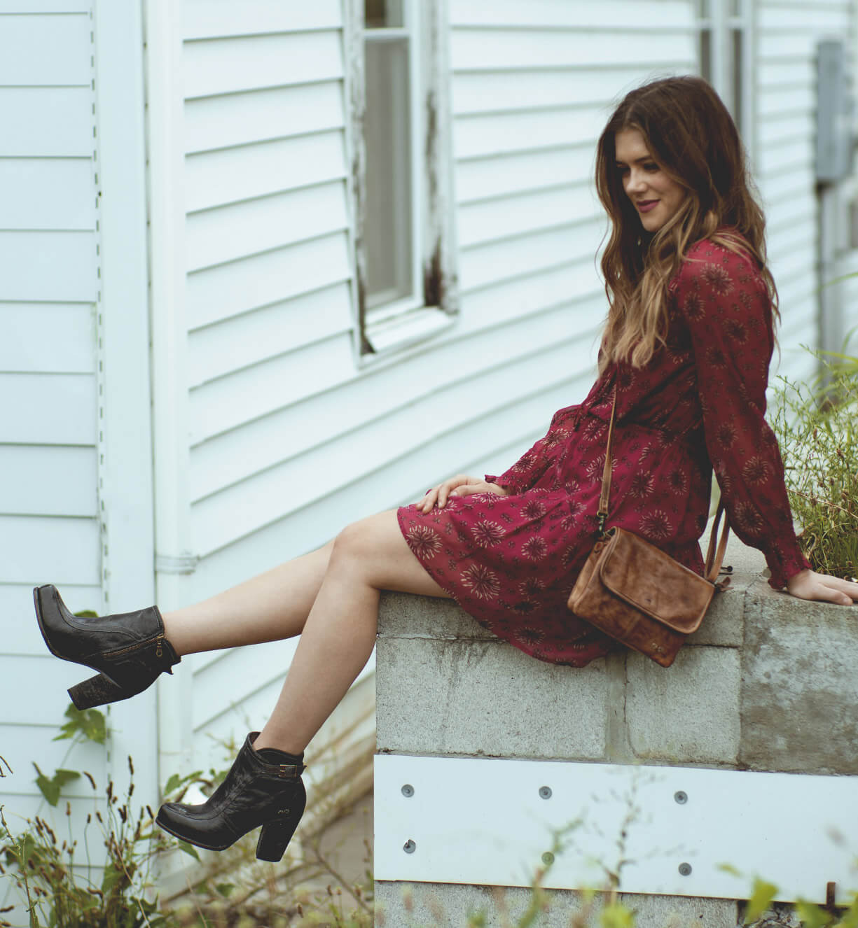A woman in a Burgundy dress sitting on a wall wearing isla boots. (Brand Name: Bed Stu)