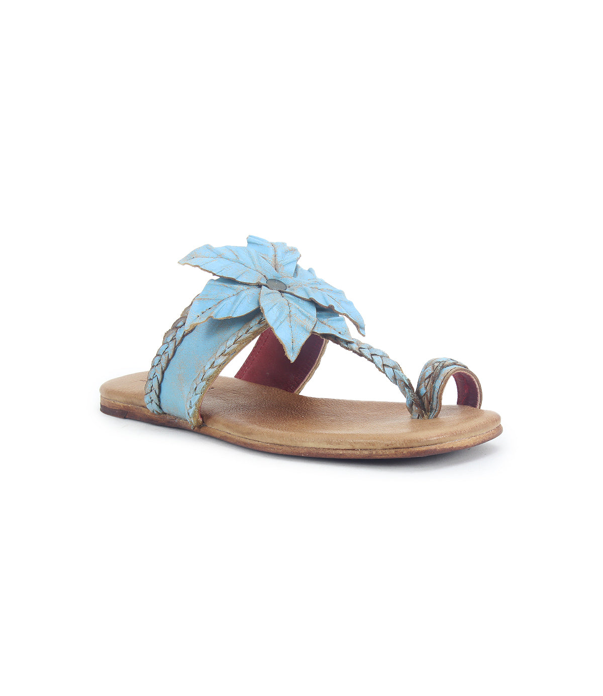 The Bed Stu Isobel is a flat sandal with a tan sole, light blue braided leather straps, and a large blue leaf-shaped decoration on top.