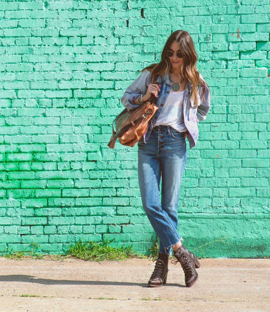 A woman wearing Izetta jeans and a Bed Stu denim jacket in front of a green wall.