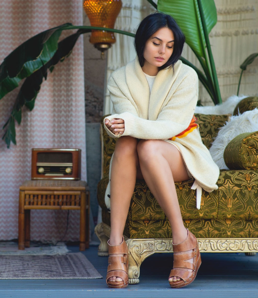 A woman sitting on a couch in a white sweater and Bed Stu Jacey II sandals.