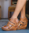 A woman wearing Bed Stu Jacey II wedge sandals on a wooden floor.