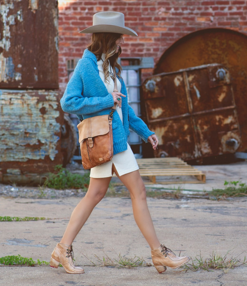 A woman wearing hat, blue cardigan, and Jack bag by Bed Stu while walking down a street.