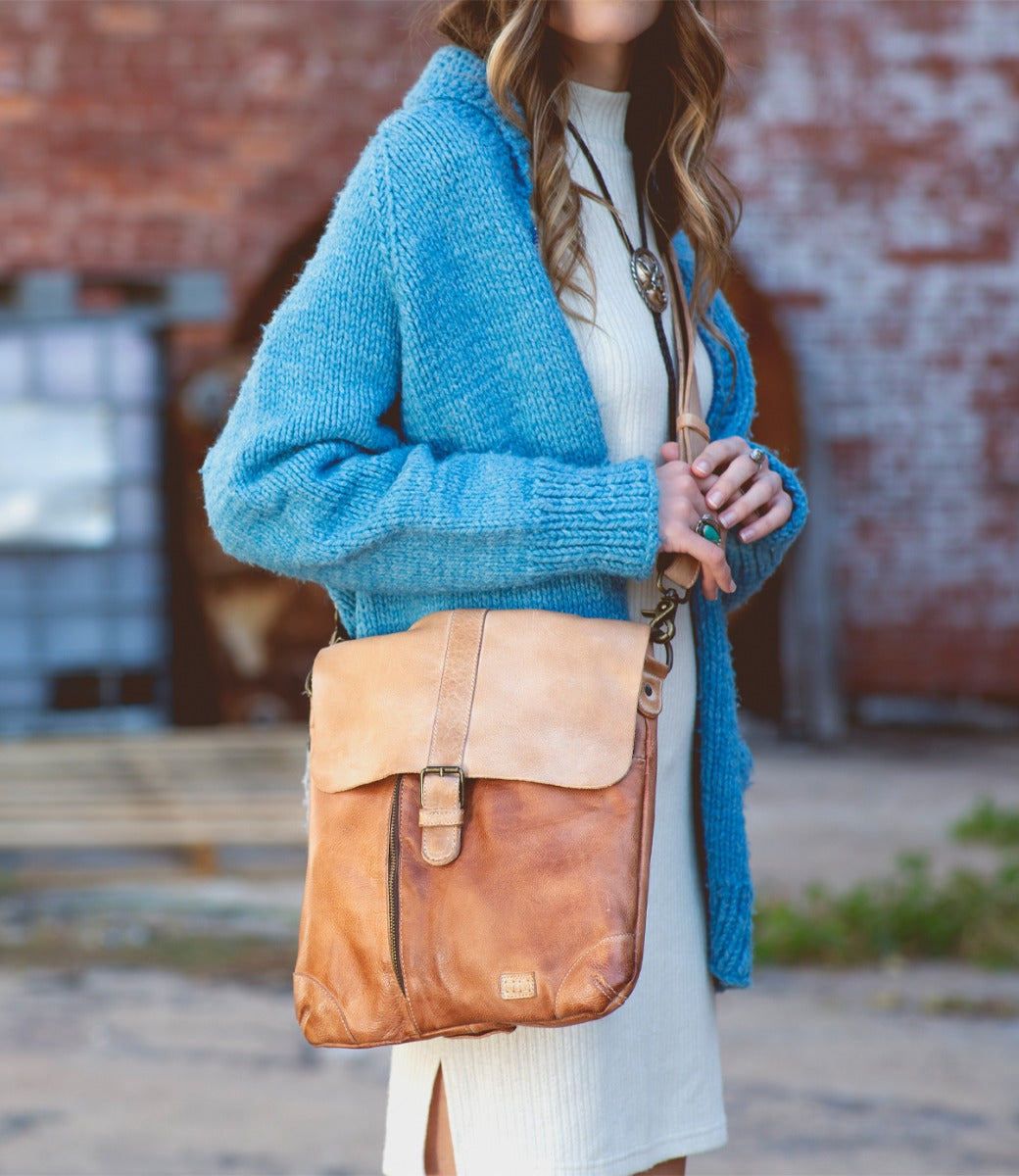 A woman wearing a blue dress and a tan Jack bag by Bed Stu.