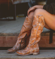 A woman is sitting on a wooden bench wearing Bed Stu Jacqueline boots.
