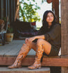 A woman sitting on a porch in a pair of Bed Stu Jacqueline cowboy boots.