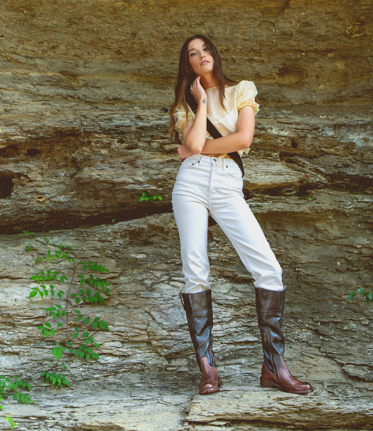 A woman in white Jacqueline jeans and Bed Stu boots standing on a rock.