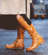 A woman wearing tan leather Bed Stu Jacqueline Wide Calf boots and a trench coat.