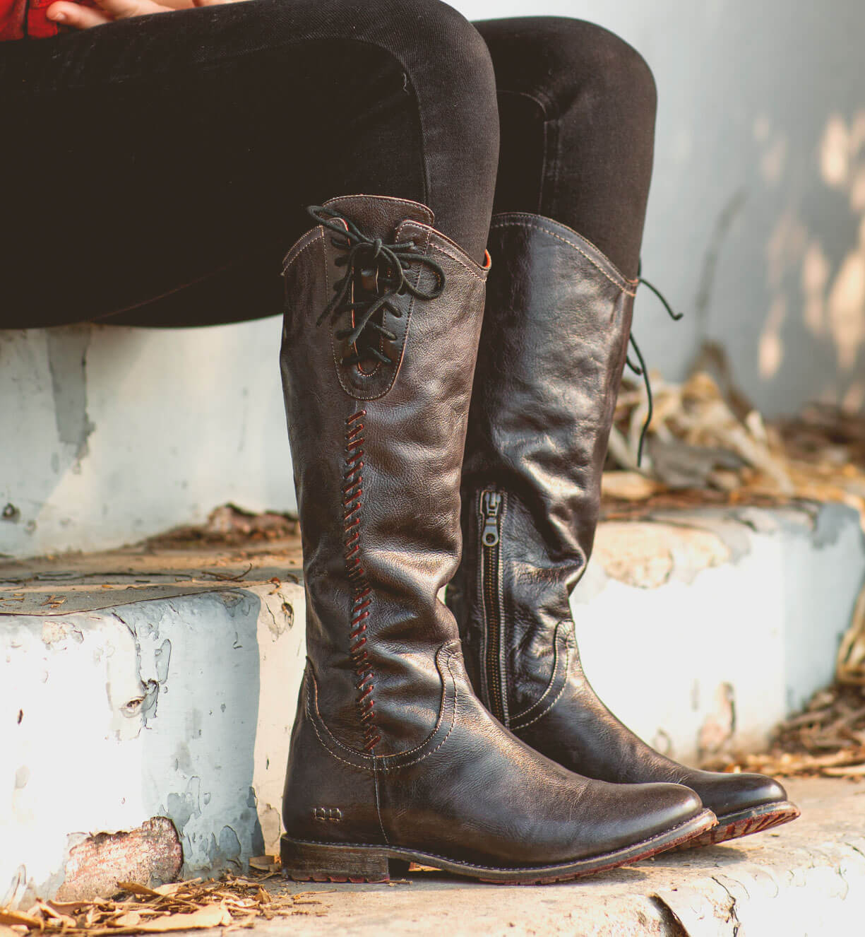 A woman is sitting on steps in a pair of Bed Stu Janina boots.