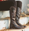 A woman is sitting on steps in a pair of Bed Stu Janina boots.
