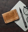 A Jeor wallet with glasses and a notebook on a wooden table. (Brand: Bed Stu)