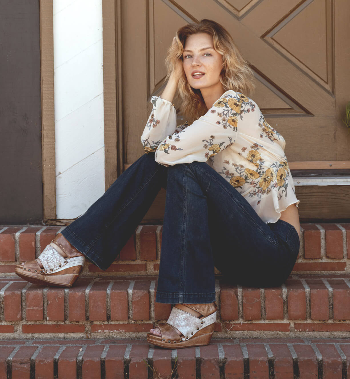 A woman sitting on the steps of a house wearing Jessie jeans and a Bed Stu blouse.