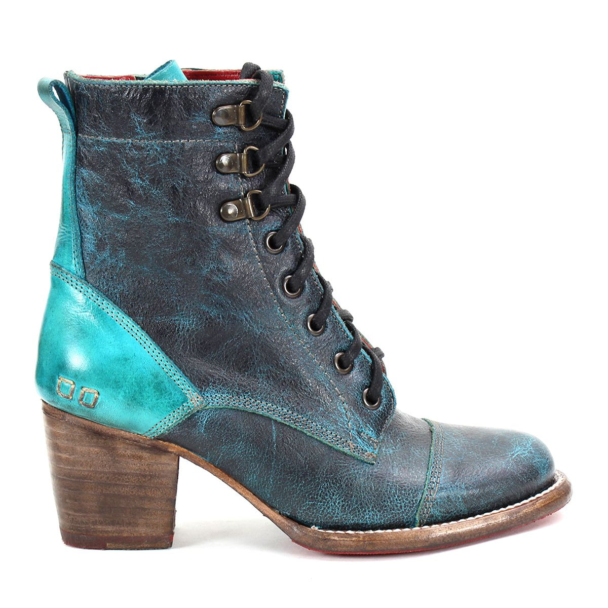 The Judgement boot by Bed Stu showcases a worn-look teal and dark blue leather design with an 8-eye lace-up, chunky wooden heel, metallic details, cushioned insole, and a cap-toe finish.