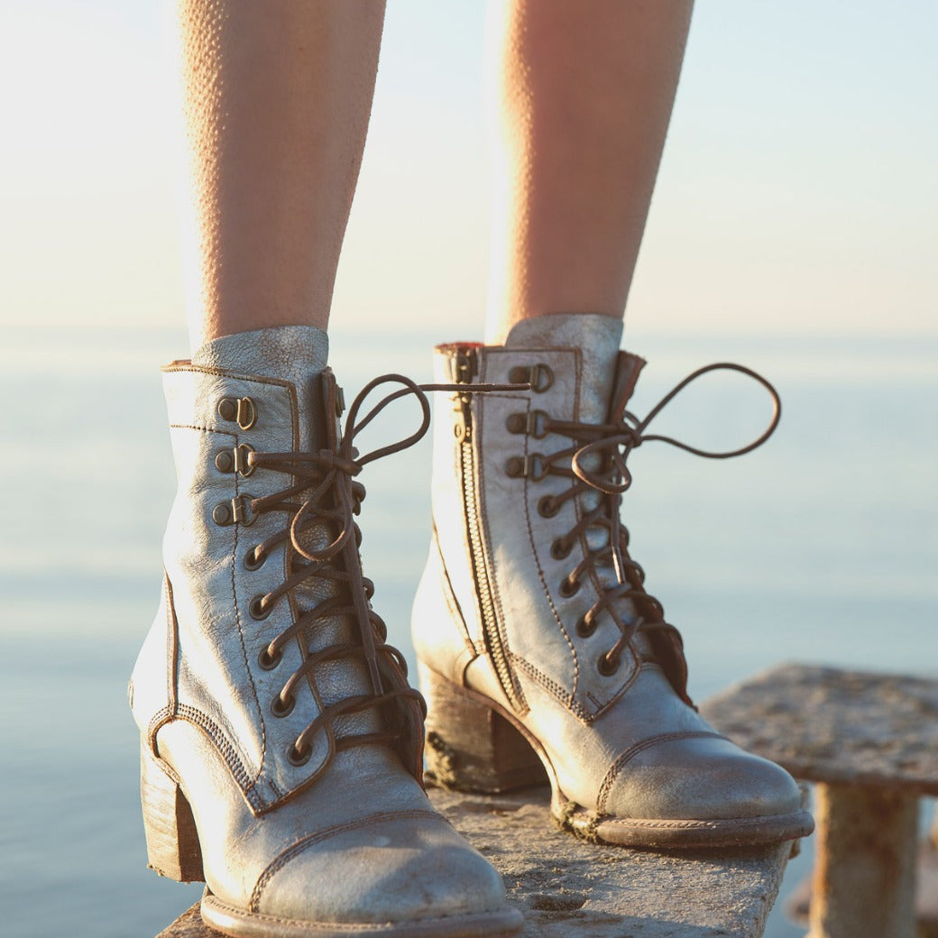 A woman's legs standing on a railing next to the ocean, wearing the Judgement shoes by Bed Stu.