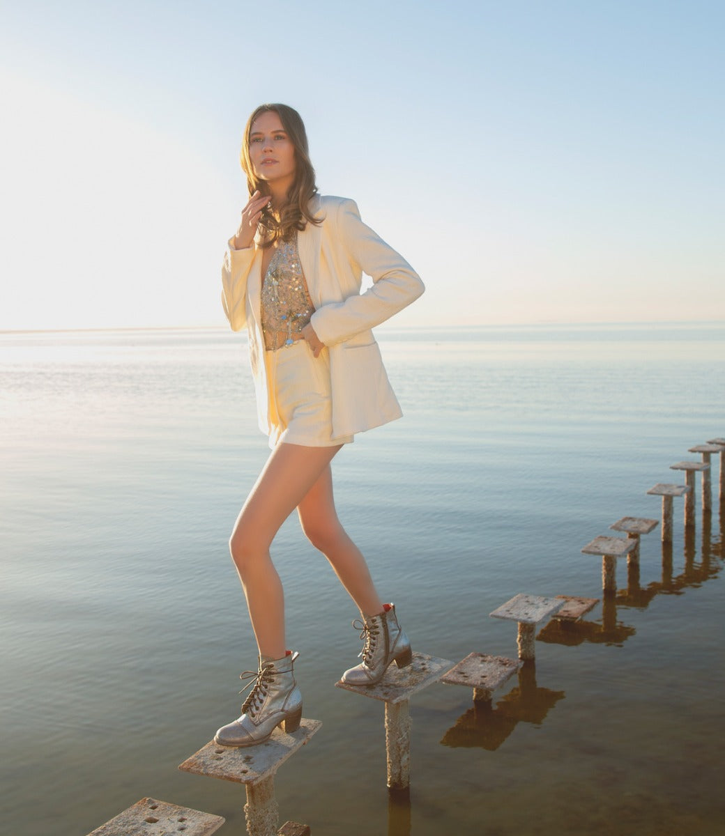 A woman in a white Bed Stu blazer and shorts standing on a dock.