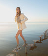 A woman in a white Bed Stu blazer and shorts standing on a dock.