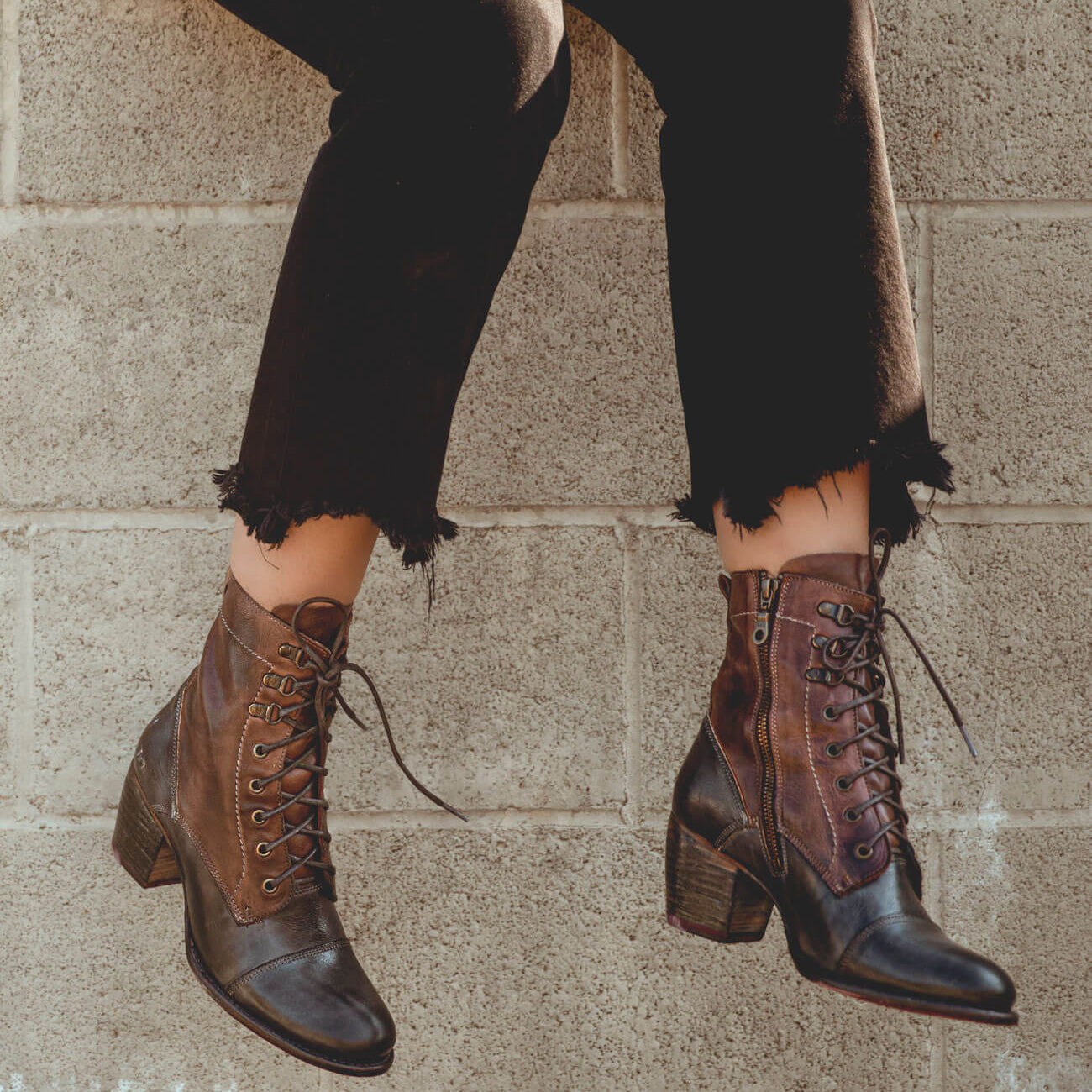 A woman is leaning against a brick wall wearing Bed Stu Judgement boots.