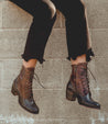 A woman is leaning against a brick wall wearing Bed Stu Judgement boots.
