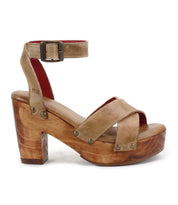 The Kalah sandal by Bed Stu features brown leather, a chunky wooden heel, an ankle strap, and metal rivet details, all crafted from sustainably sourced materials.