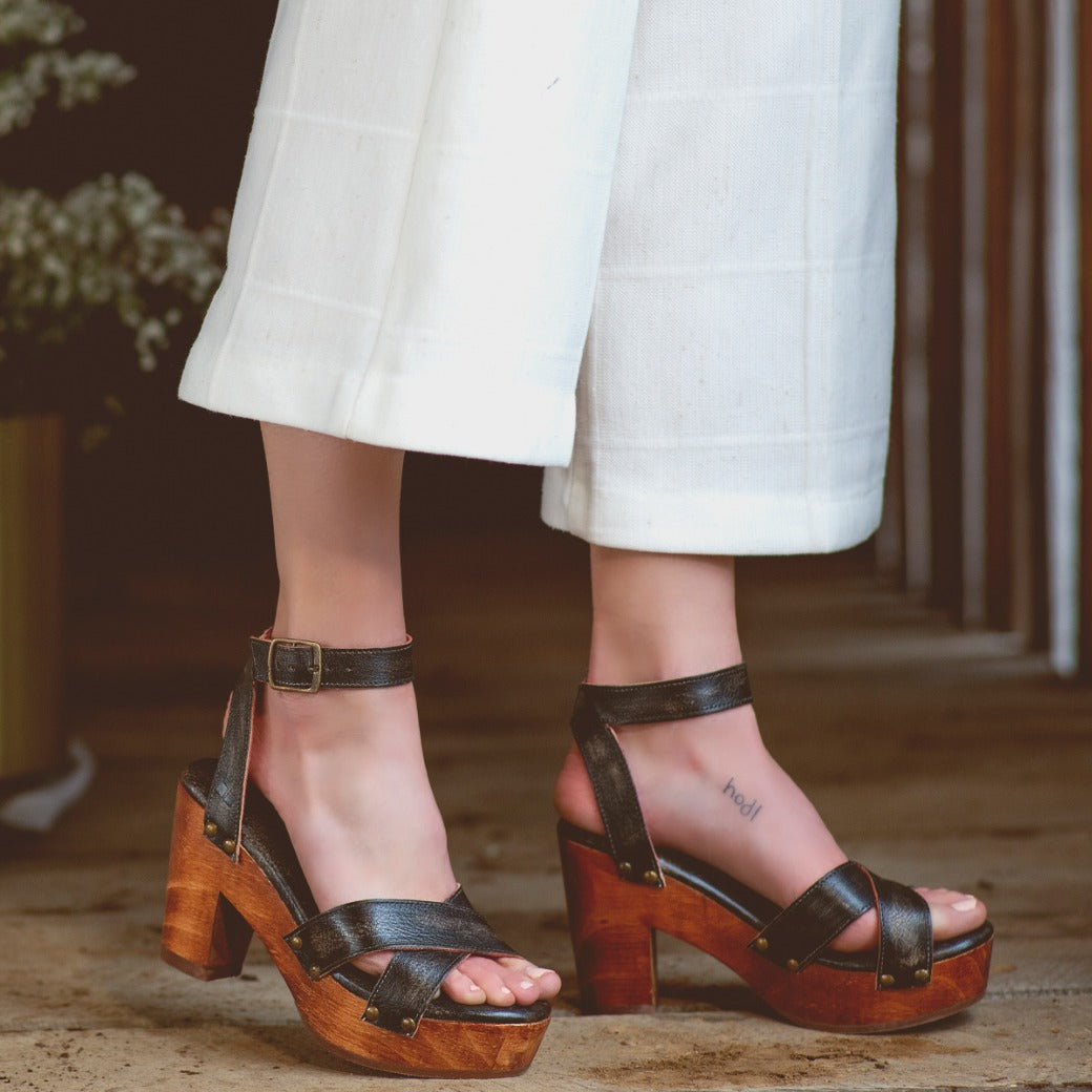 A woman wearing white pants and Bed Stu Kalah wooden sandals.