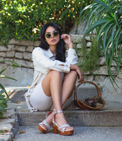 A woman in a white shirt and sandals sitting on steps wearing Kalah sandals by Bed Stu.