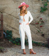 A woman wearing a white Bed Stu jumpsuit and a pink Bed Stu hat.