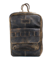 A worn, handcrafted leather backpack with a single top handle, a front pocket, and a label patch above it made from vegetable-tanned leather. The Kamet by Bed Stu.