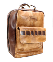 A handcrafted brown leather backpack with a large front pocket and a handle on top. The Kamet by Bed Stu, made from vegetable tanned leather, features a brand label and a zipper running around the sides.