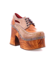 A single tan leather Bed Stu Karaoke shoe with brown laces and a decorative wavy chunky wooden platform, adorned with metallic rivets around the bottom edge, channels that 70s era flair.