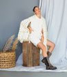 A woman wearing a white shawl and Kataleya by Bed Stu boots sitting on a wooden box.