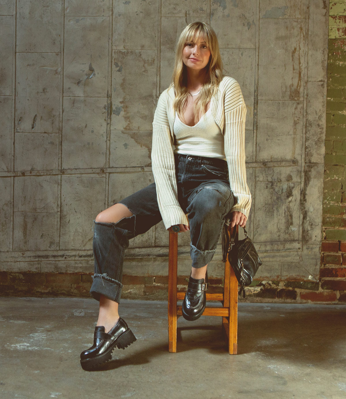 A woman is sitting on a wooden chair wearing Bed Stu leather loafers, showcasing fall fashion and comfort.