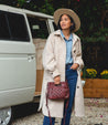 A woman is standing in front of a van wearing jeans, a hat, and Bed Stu Keiki.