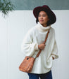 A woman wearing a white sweater and a burgundy hat with a tan Keiki bag.
