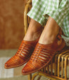 A woman's feet sitting on a wicker chair wearing Bed Stu Kennya sandals.