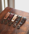 Five Bed Stu Keygrab leather keychains on top of a wooden table.