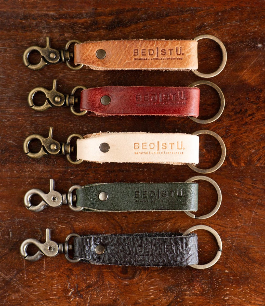 Five Bed Stu Keygrab leather keychains on a wooden table.