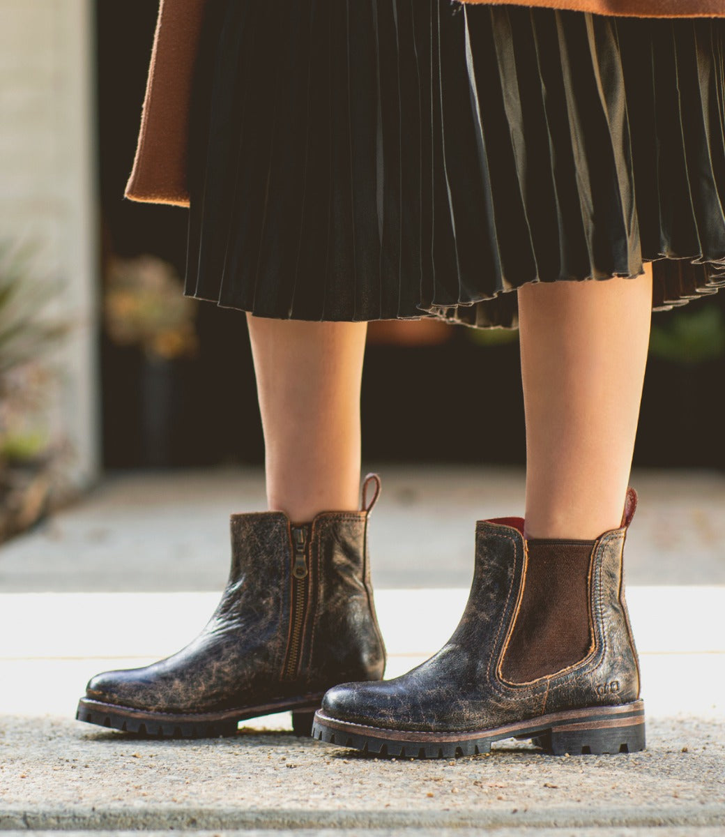 A woman wearing Kiefra by Bed Stu brown leather boots and a pleated skirt.