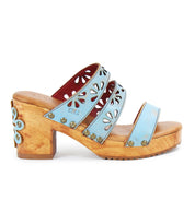 The Bed Stu Kreep is a wooden platform sandal with light blue leather straps and 70's-inspired floral cutouts, highlighted by a small flower detail on the heel.