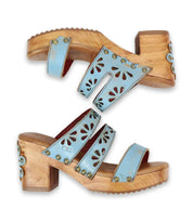 A pair of 70's-inspired "Kreep" light blue open-toed sandals by Bed Stu, featuring floral cutouts and wooden block heels, displayed side by side against a white background.
