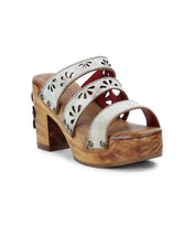 The Kreep by Bed Stu is a wooden platform sandal with a 70's-inspired design, featuring three white straps embellished with floral cutouts and silver studs.