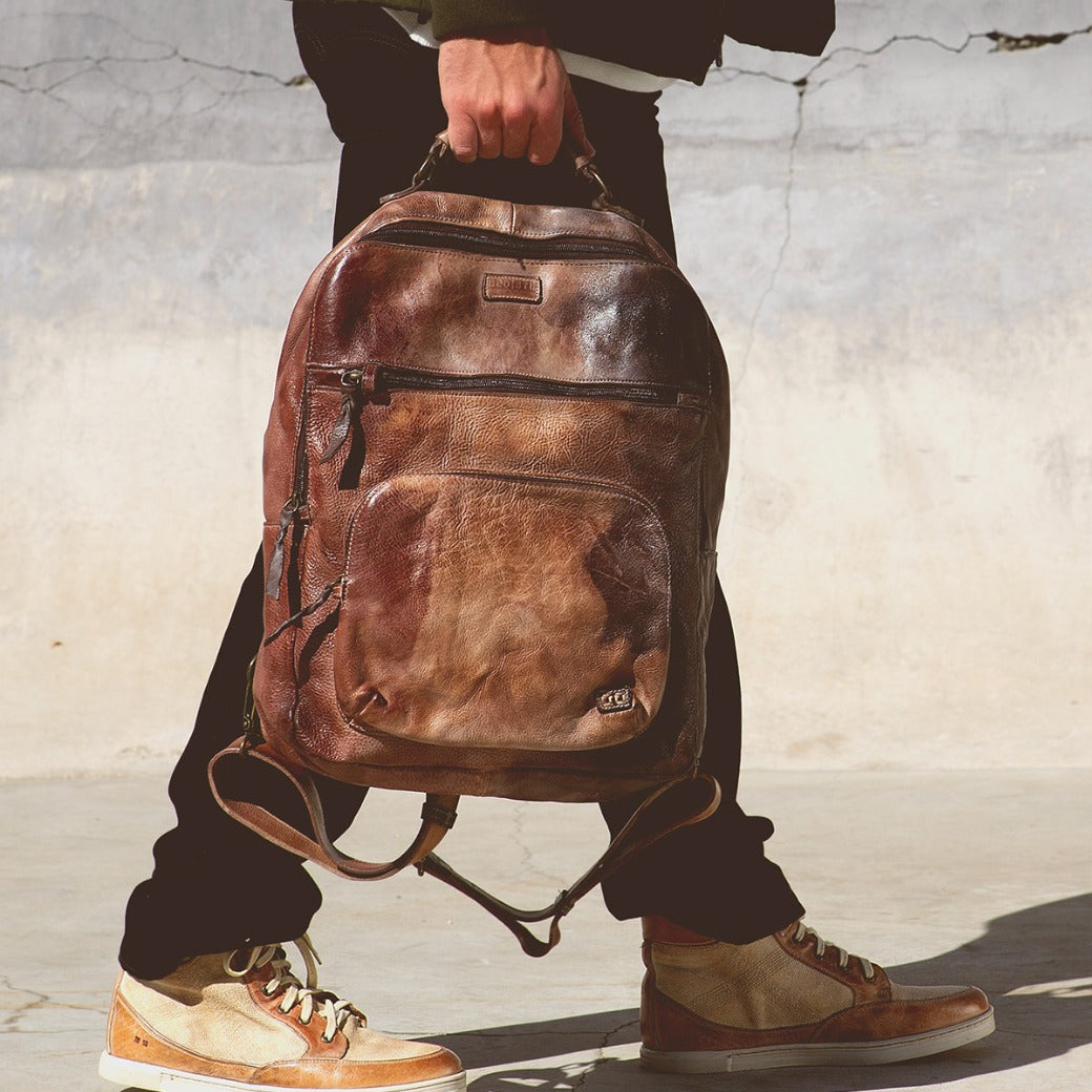 A person carrying a brown leather Bed Stu Lafe backpack.