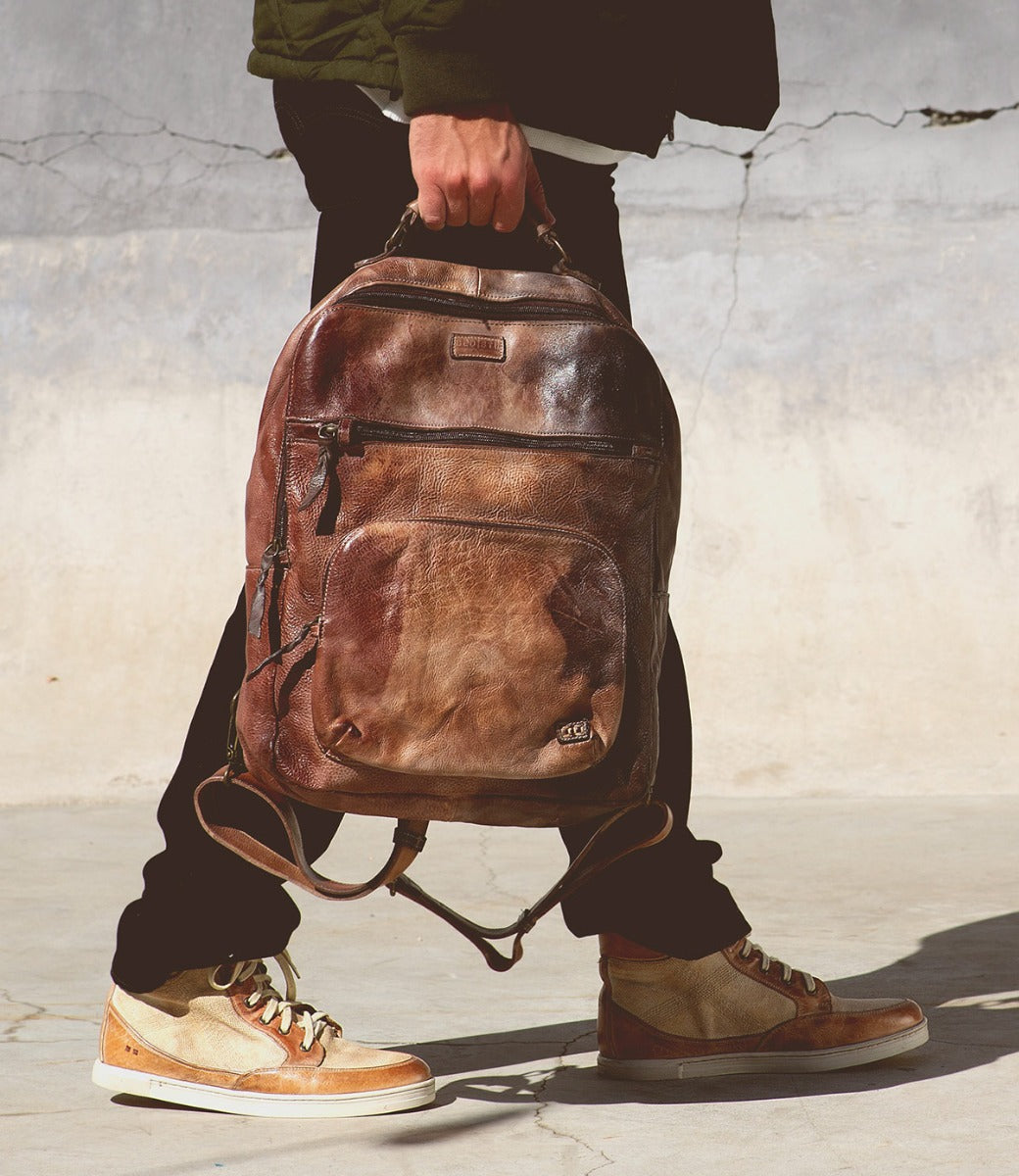 A person carrying a brown leather Bed Stu Lafe backpack.