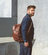 A man wearing jeans and a brown leather Bed Stu Lafe backpack.
