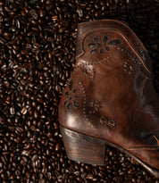 Bed|Stü Laredoa brown leather ankle boot with a floral motif stitched onto the side, laid on a bed of coffee beans.