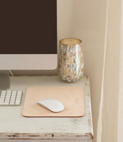 A computer monitor, keyboard, and mouse on a white wooden desk with a beige leather **Launcher Mouse Pad by Bed Stu** featuring a suede underside and a decorative cup create a curated workspace.