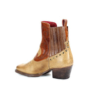 The Bed Stu League boot is a tan and brown leather Western boot adorned with decorative stitching and stud details, featuring a low heel and a pull tab on the back.