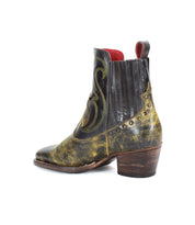 The League by Bed Stu is a distressed black and yellow leather Western short boot that features a Cuban heel, side elastic panels, playful stitching, and brass studs, exuding rugged charm.