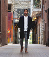 A man standing in an alleyway wearing a Bed Stu Leonardo coat and a tee shirt.