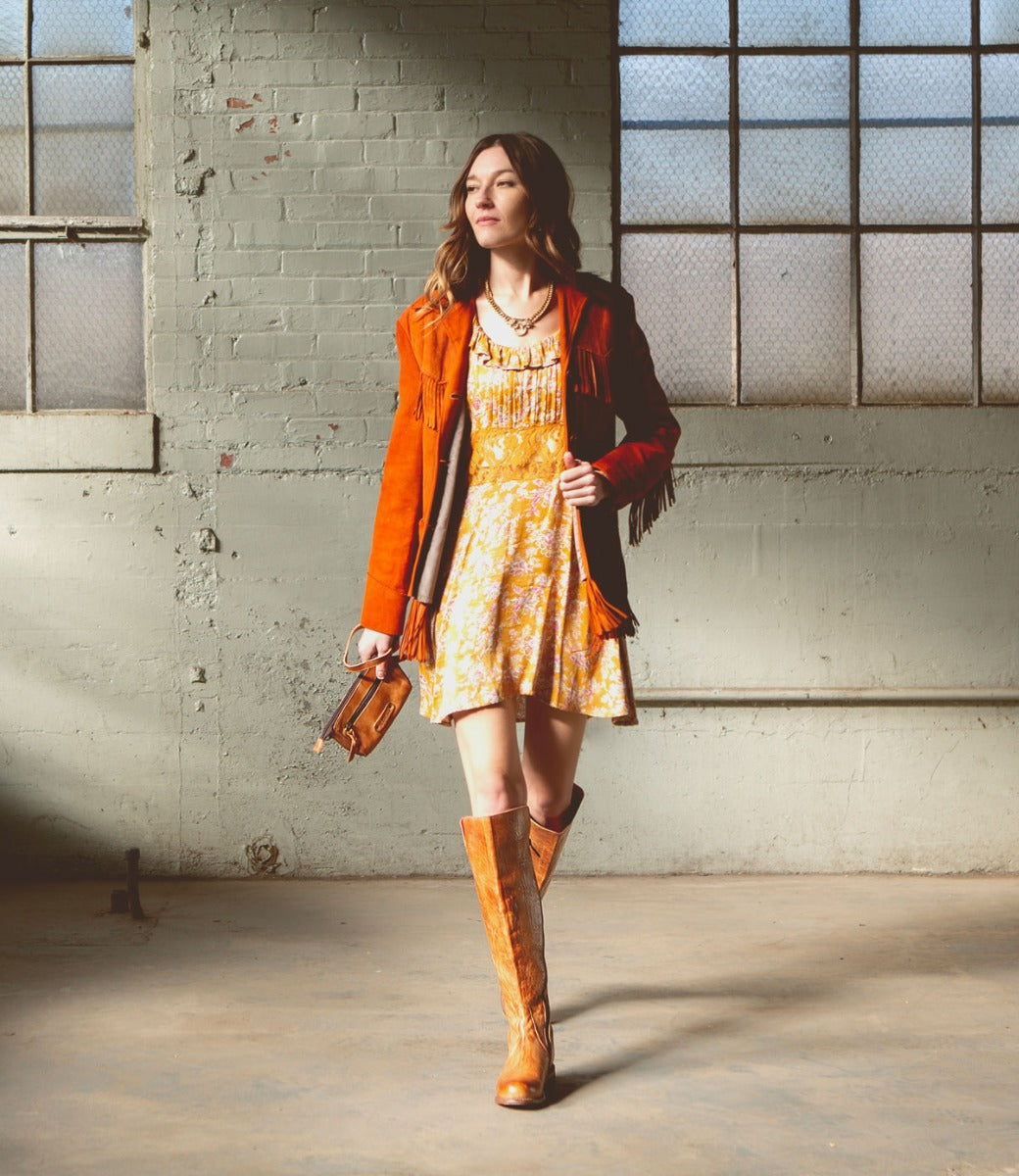 A woman in a yellow dress and Bed Stu tall boots.